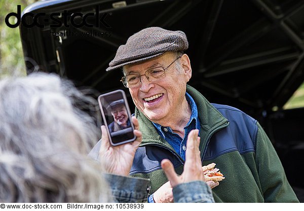 Seniorin beim Fotografieren von lächelndem Mann im Freien